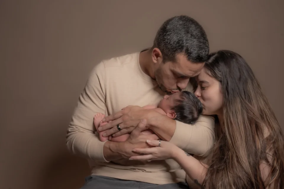 Parents leaning close around their sleeping newborn