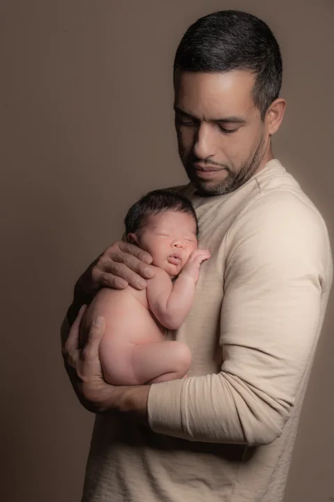 Father holding a sleeping newborn against a warm backdrop