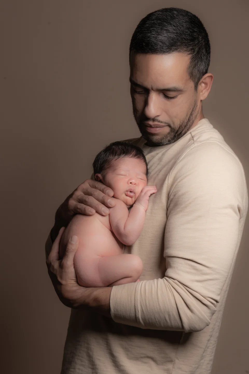 Father holding a sleeping newborn against a warm backdrop