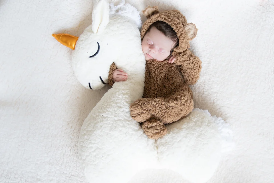 Sleeping baby in a knitted outfit beside a plush unicorn