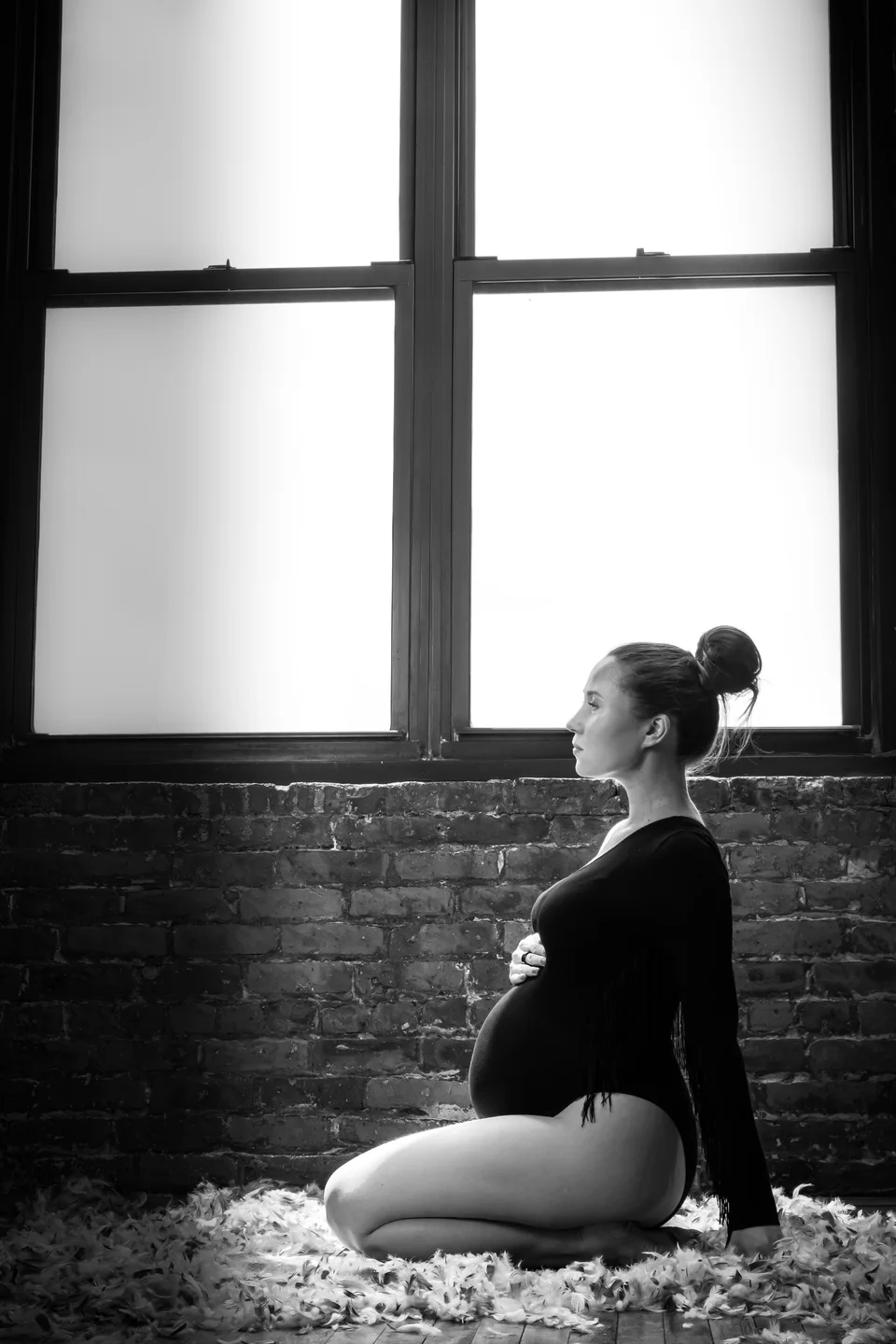 Black-and-white seated maternity portrait by a loft window