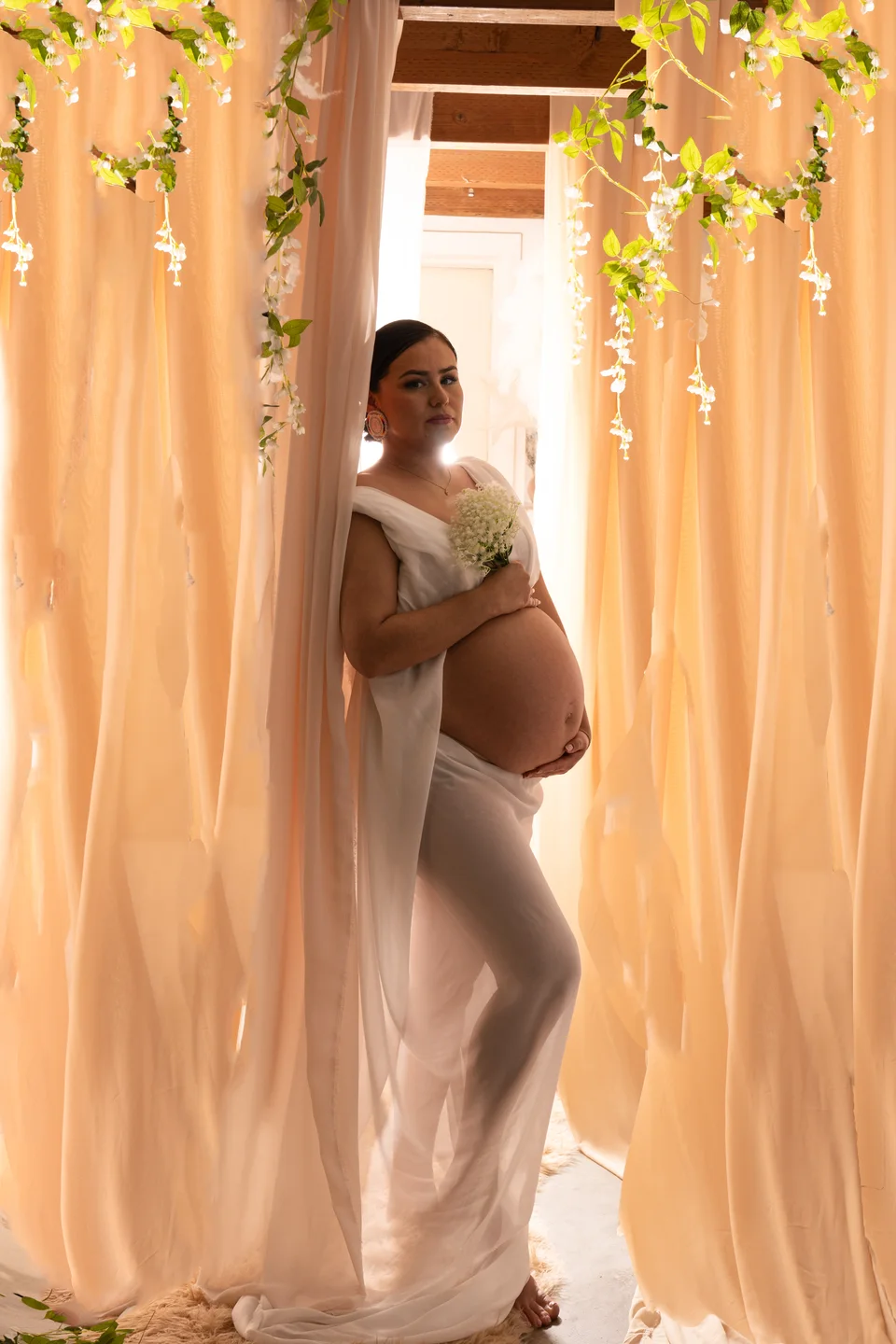 Maternity portrait surrounded by pale curtains and hanging greenery