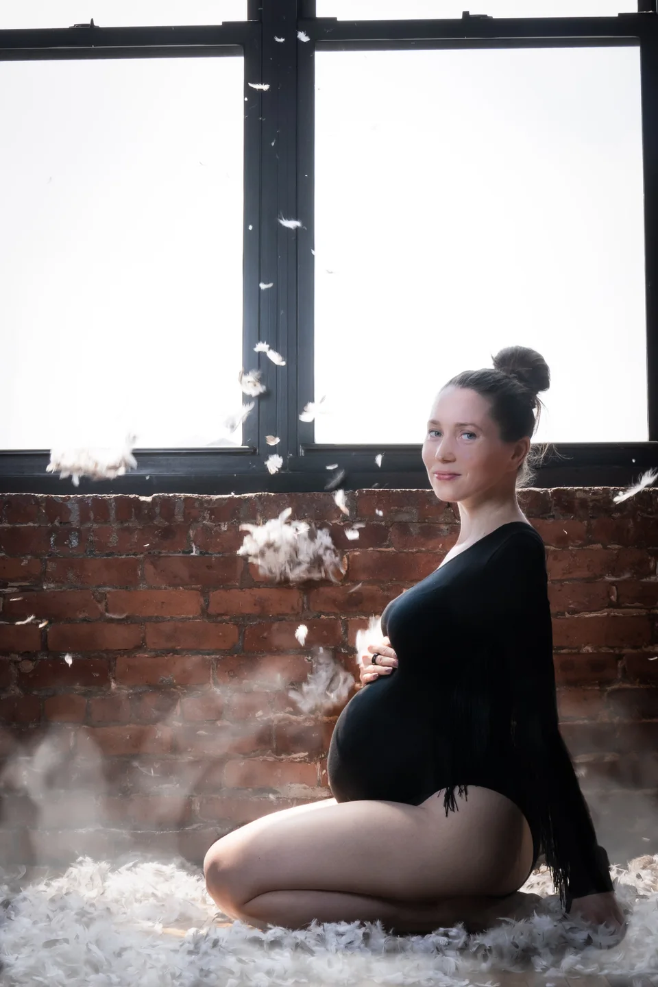 Maternity portrait seated by a window with soft haze