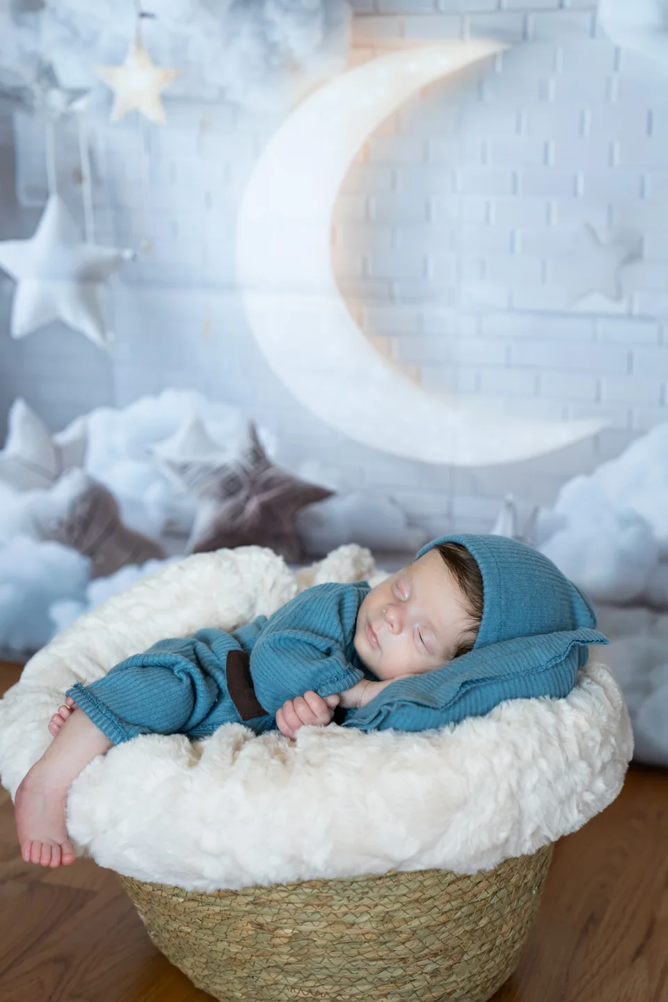 Newborn in blue sleeping in a basket beneath a moon prop