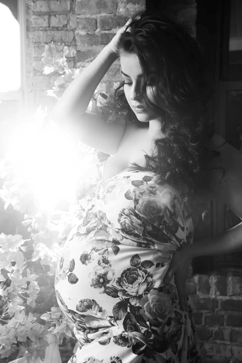 Black-and-white maternity portrait in a floral gown with backlight