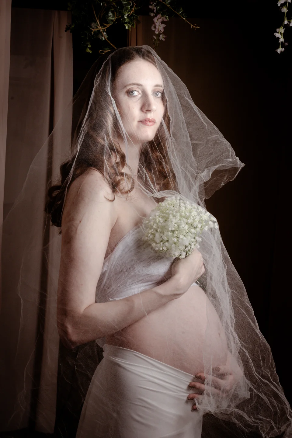 Maternity portrait with a sheer veil and pale flowers