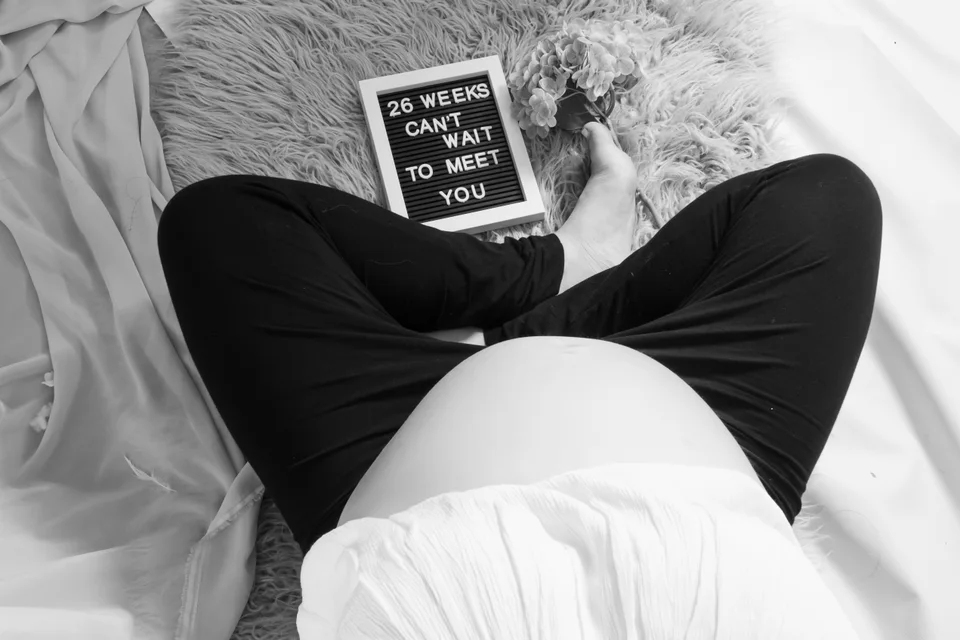 Overhead black-and-white maternity portrait with a letter board
