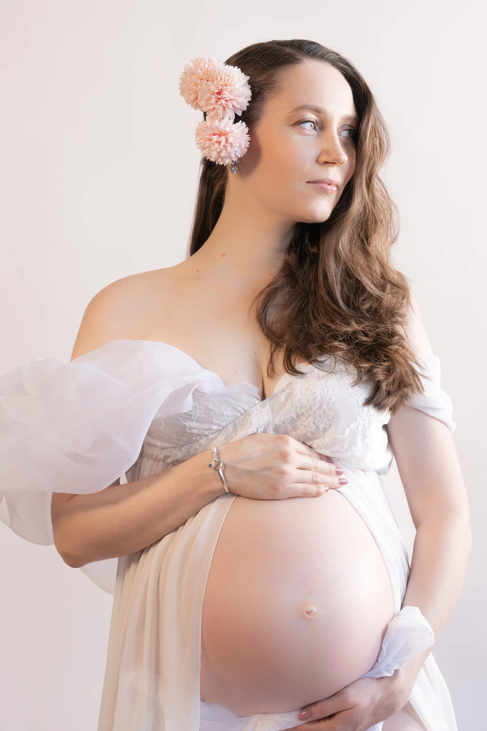 Maternity portrait with white fabric and a pink flower in her hair