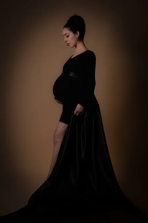 Maternity portrait in a long black gown against a warm backdrop